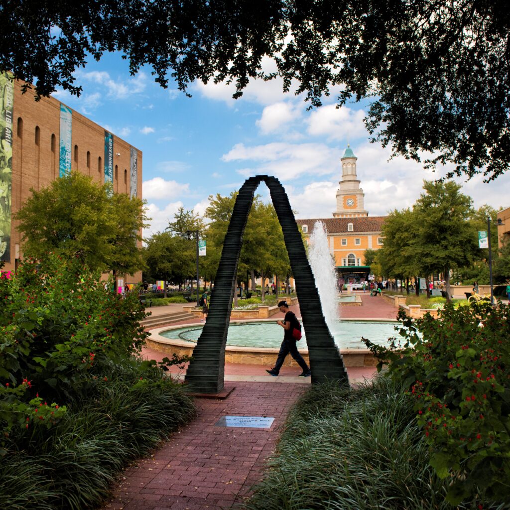 Image of UNT campus, water fountain, and student walking by.
